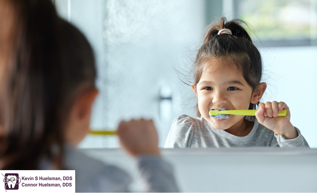Young girl brushing her teeth while looking in a mirror.