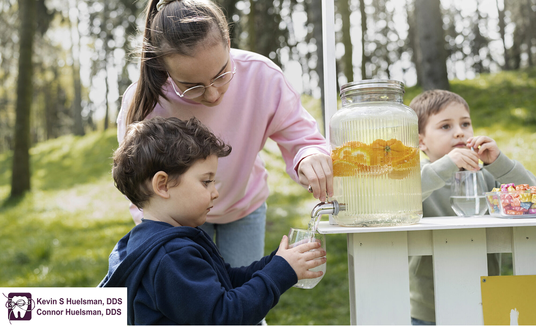 Young child asking for juice from a jar, assisted by an older sister.